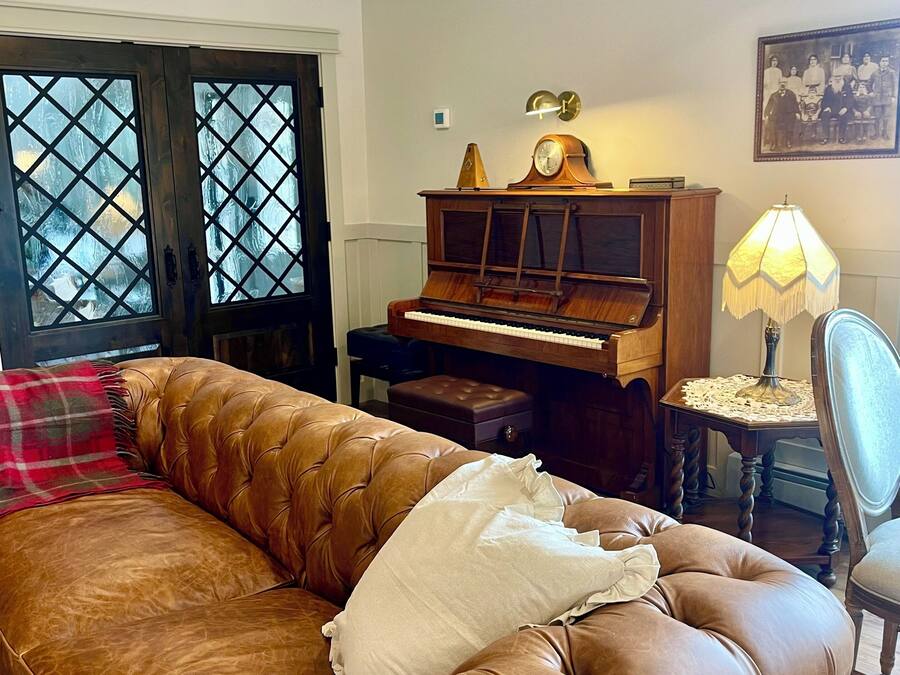Uma sala de estar com um sofá de couro marrom, um piano de madeira e um abajur de renda.