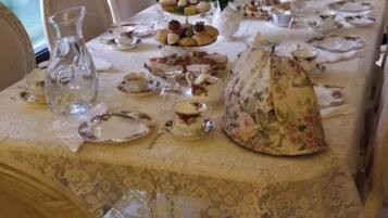 Une table à manger dressée avec des assiettes, des verres et un pichet, entourée de chaises dans une pièce dotée d’une fenêtre et de rideaux.