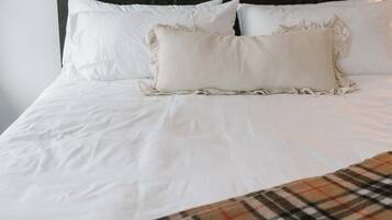 A neatly made bed with white linens and a plaid throw blanket.