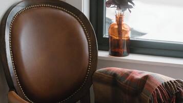 A brown leather chair with a plaid throw blanket, positioned by a window with a view of a snowy landscape.