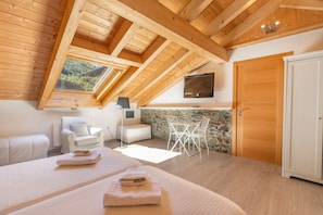 Une chambre avec un plafond en pente, un téléviseur fixé au mur, un mur en pierre et une porte en bois.