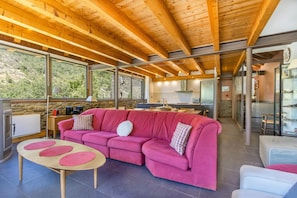 A modern interior with a wooden ceiling, a pink sofa, a round table, and large windows offering a view of the outdoors.