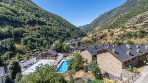 Paesaggio montano con piscina, edifici in pietra e parcheggio.