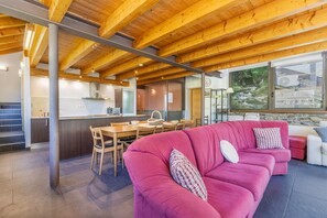A modern interior with a wooden ceiling, a pink sofa, a dining area, and a kitchen.