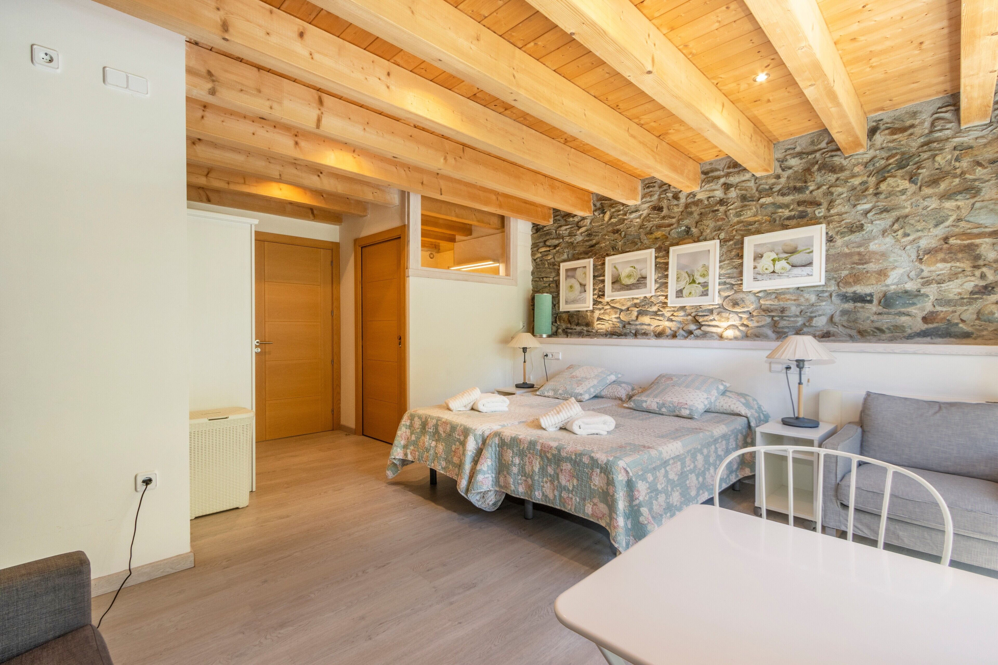 A bedroom with a wooden ceiling, a stone wall, and a bed with a floral bedspread.