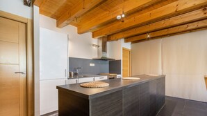 Une cuisine moderne dotée d’un îlot central, de poutres en bois au plafond et d’un revêtement de sol en carreaux de couleur sombre.