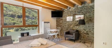Un dormitorio con una ventana grande, una cama, un escritorio, una silla, un televisor y una pared de piedra.