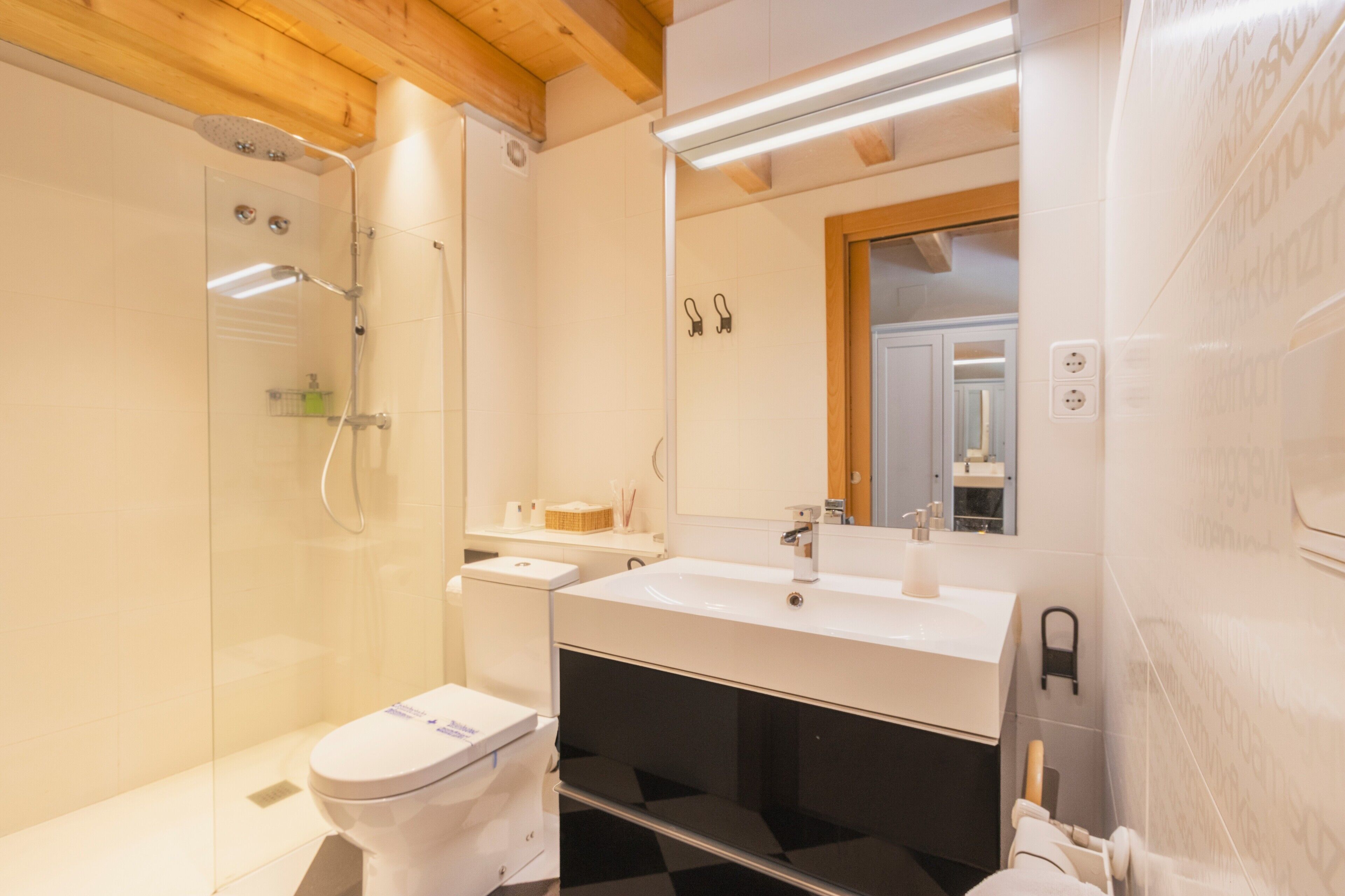 Un baño con cabina de ducha de vidrio, un inodoro blanco, un lavabo con espejo y un perchero para toallas.