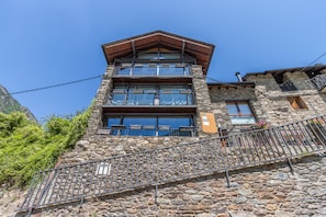 A multi-story stone building with balconies, a staircase, and a mountain backdrop.