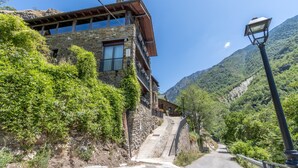 Un bâtiment en pierre doté d’un balcon, d’un escalier menant à l’étage supérieur et, en arrière-plan, une montagne.
