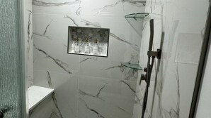Un espace douche moderne doté d’une paroi en verre, d’un pommeau de douche à main et d’un sol carrelé à motifs de marbre.