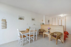 Una stanza moderna e minimalista con un tavolo da pranzo in legno, sedie bianche, una poltrona in vimini, un piccolo tavolino e un divisorio in legno.