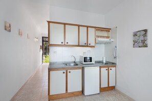 Una cocina compacta con armarios blancos, microondas integrado, lavamanos y un refrigerador pequeño.