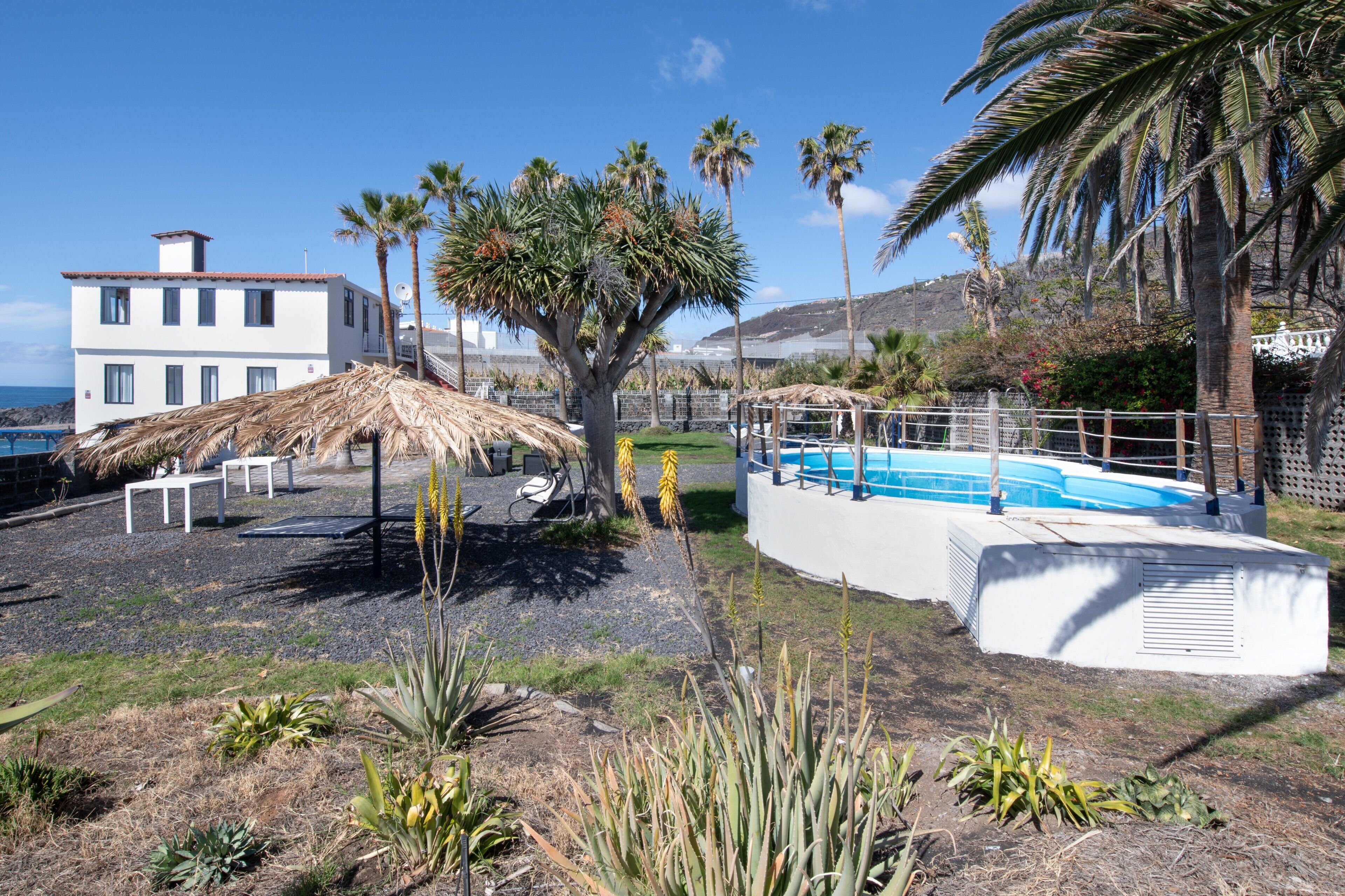 Ein Poolbereich mit einem weißen Pool, Palmen und einem Gebäude mit weißer Fassade.