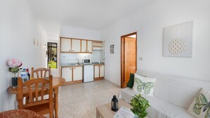 Un espace de vie compact comprenant un coin cuisine, un coin repas et un espace détente avec un canapé et des coussins.