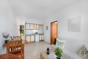 Un espacio habitable compacto con kitchenette, comedor y zona de estar con sofá y cojines.