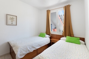 A bedroom with two single beds, a wooden nightstand, a window with curtains, and a framed picture on the wall.