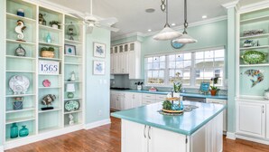 A spacious kitchen with white cabinets, a teal countertop, and various decorative items. - The Beach Escape (St. Augustine)