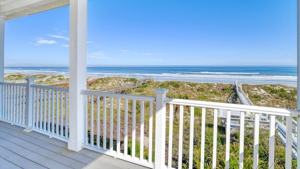 A covered deck with white railings overlooking a beach with dunes and a clear blue sky. - The Beach Escape (St. Augustine)