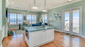 A spacious kitchen with a large island, multiple windows offering ocean views, and a ceiling fan. - The Beach Escape (St. Augustine)
