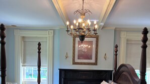 A bedroom with a four-poster bed, a chandelier, a fireplace, and a window with a view.