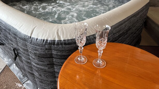 A hot tub with two clear glasses on a wooden table.