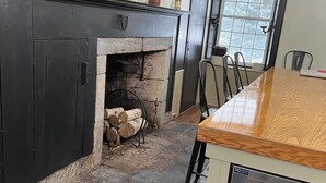 A kitchen with a stone fireplace, wooden flooring, and a stainless steel refrigerator.