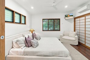 A bedroom with a bed, a chair, a window, and a ceiling fan.