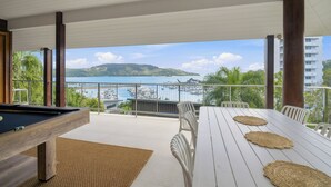 Una mesa de billar en un balcón con vistas a un puerto deportivo y una isla distante.