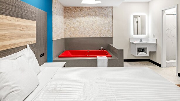 A modern hotel room with a large bed, a red bathtub, a white sink, and a mirror above the sink. - La Mirage Inn - Long Beach (Long Beach)
