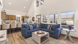A modern living room with a blue sectional sofa, a coffee table, and a kitchen area with wooden cabinets and a bar stool. - Dog Friendly Bungalow in the heart of Dover Bay (Dover)