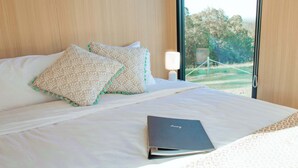 A bed with patterned pillows, a book, and a nightstand with a lamp. - Amaroo One by Tiny Away (Minimbah)