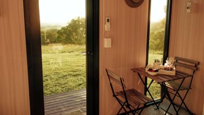A wooden room with a table and chairs, a hat on the wall, and a view of a grassy field. - Amaroo One by Tiny Away (Minimbah)