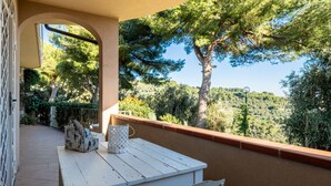 Un balcon avec une table et une chaise, donnant sur un paysage luxuriant, avec des arbres et une colline en arrière-plan.