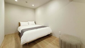 A bedroom with a bed, a small ottoman, and a ceiling light fixture. - Vibrant 1BR, Downtown, Shopping & Dining Nearby 11 (Hiroshima)