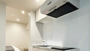 A compact kitchen with a built-in stove, a small sink, and a microwave. There is a wooden floor and a bed in the adjacent room. - Vibrant 1BR, Downtown, Shopping & Dining Nearby 11 (Hiroshima)