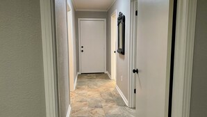 A hallway with a white door at the end, a mirror on the wall, and a tiled floor. - Charming, newly remodeled 2-bedroom duplex near Carthage w/ AC, fast WiFi (Carthage)