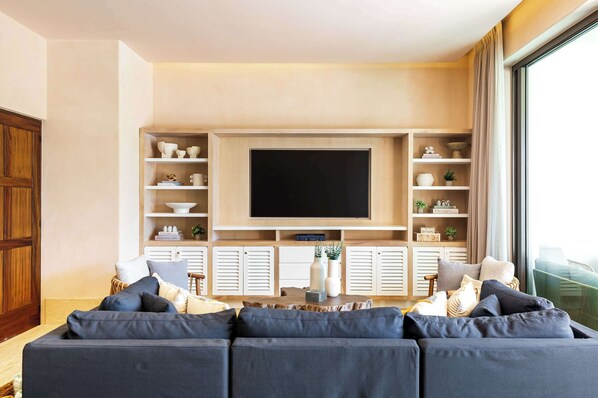 A modern living room with a large flat-screen TV mounted on a wooden wall, a dark-colored sofa, and a coffee table with decorative items.