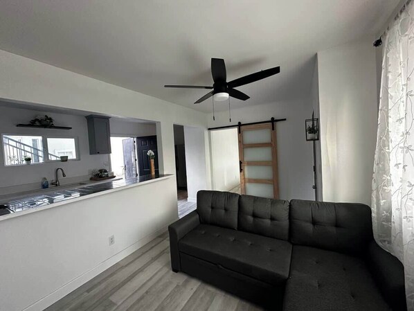 Un espacio habitable moderno con cocina, sofá, ventilador de techo y puerta corredera.