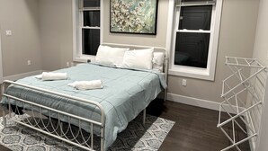 Un dormitorio con cama, dos ventanas, un cuadro y un tendedero.