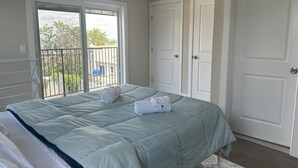 Un dormitorio con cama, balcón y dos puertas blancas.