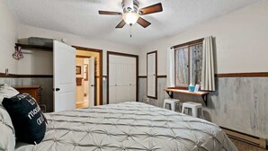 Un dormitorio con una cama, ventilador de techo, escritorio con silla y ventana con cortinas.