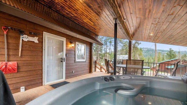 Una cabaña de madera con jacuzzi en el porche, una puerta y una mesa con sillas.