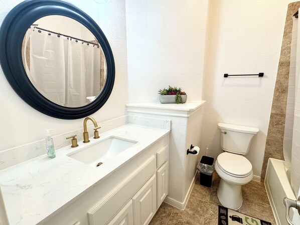 Une salle de bain avec un meuble-lavabo blanc, un miroir rond, des toilettes et une baignoire.