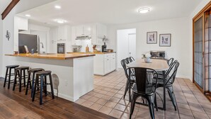 A modern kitchen with white cabinets, a wooden island, and a dining area with black chairs.