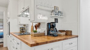 A modern kitchen with white cabinets, a wooden countertop, and a neon 'Cheers' sign.
