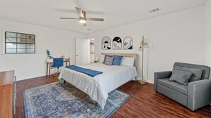 A bedroom with a bed, a desk, a chair, a floor lamp, and a ceiling fan.