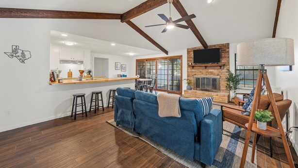 A spacious living room with a blue sofa, wooden beams, a fireplace, and a kitchen in the background.