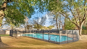 A rectangular swimming pool with a black safety fence, surrounded by a grassy yard and trees.