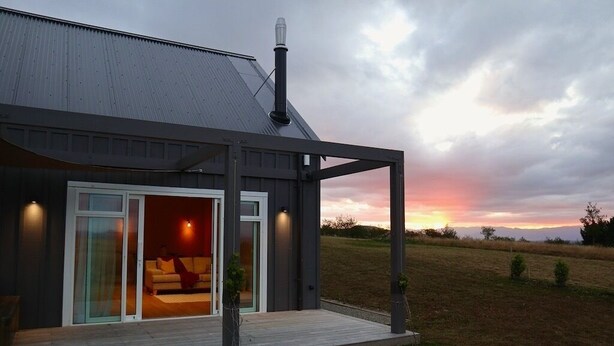 A modern house with a covered porch, a large sliding glass door leading to a living area, and a view of the sunset over a grassy field. - Beautiful Wairarapa views, short drive to all Martinborough has to offer (Martinborough)